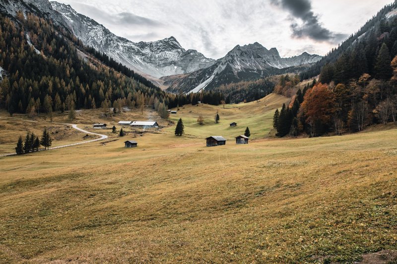 Almtal im Herbst mit Heustadeln, dahinter schroffe Berge.